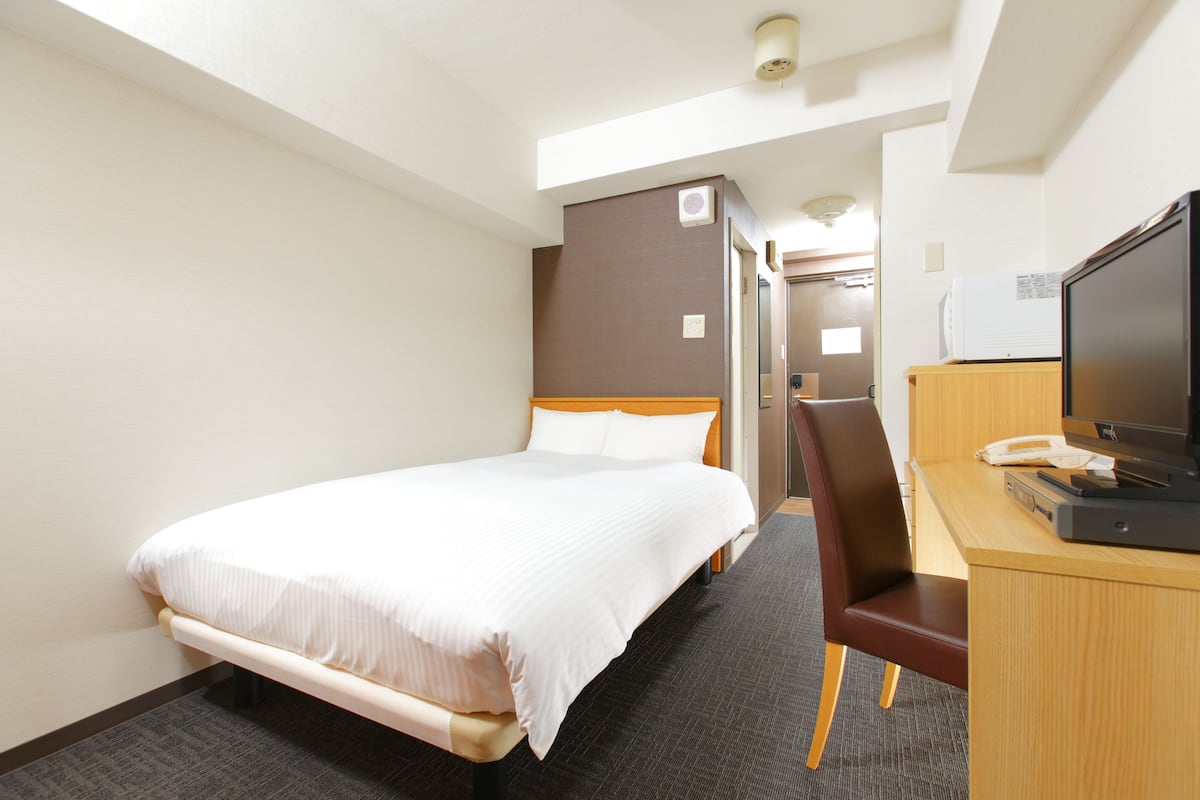 A hotel room with a bed, a desk with a television, and a chair.