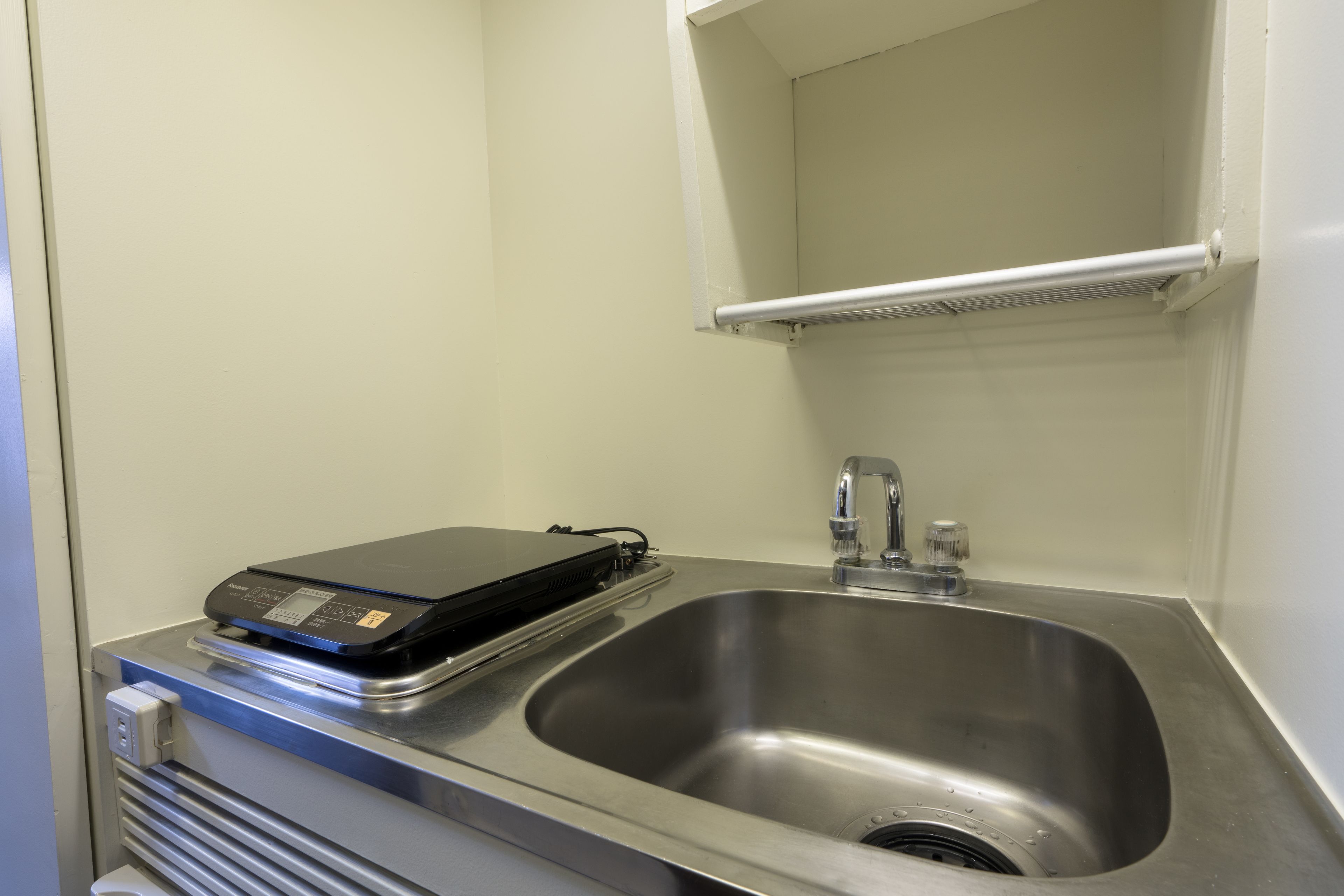 A stainless steel sink with a faucet and a black electronic device on a counter.
