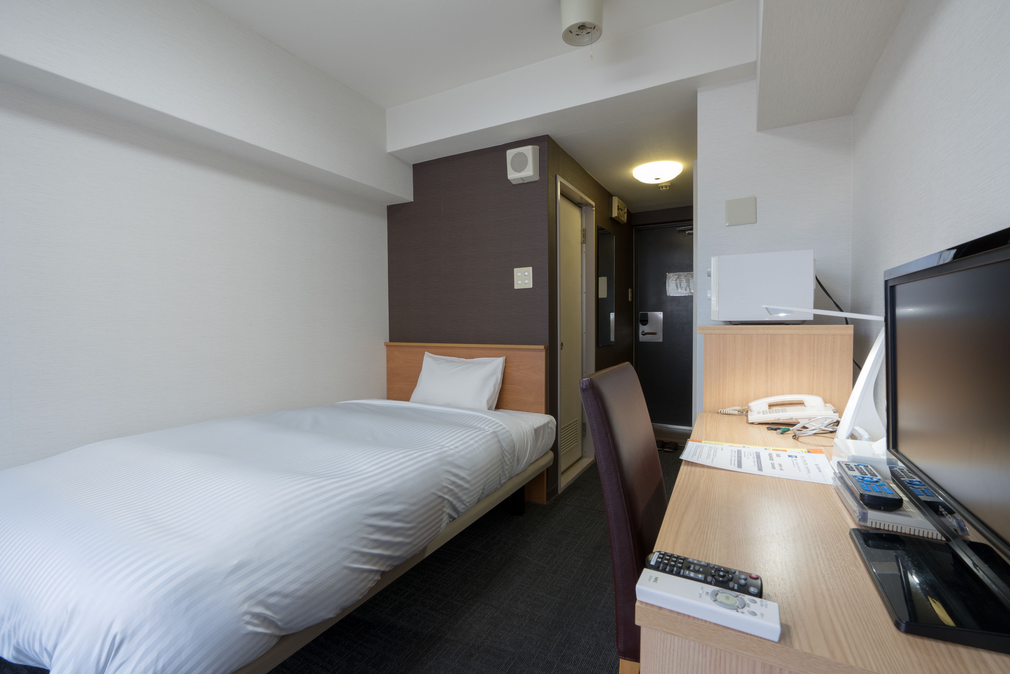 A hotel room with a single bed, a desk with a computer, a TV, and a chair.