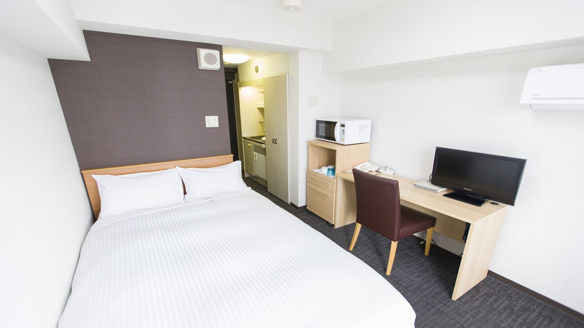 Hotellihuone, jossa on sänky, työpöytä, jossa on tietokone ja televisio, mikroaaltouuni sekä pieni keittokomero.