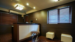 A modern reception area with a wooden reception desk, a small round table, and two white cushioned seating areas. - Flexstay Inn Shirogane (Tokyo)