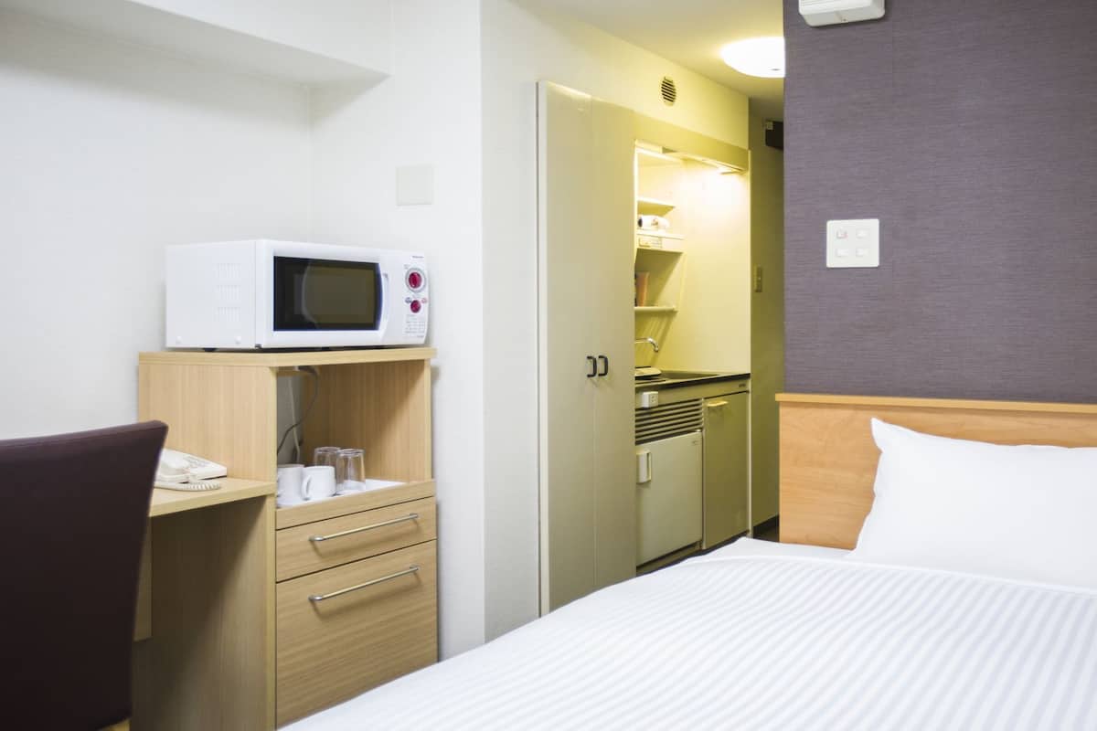 Hotellihuone, jossa on sänky, työpöytä, jossa on mikroaaltouuni, pieni keittiö ja kylpyhuone.