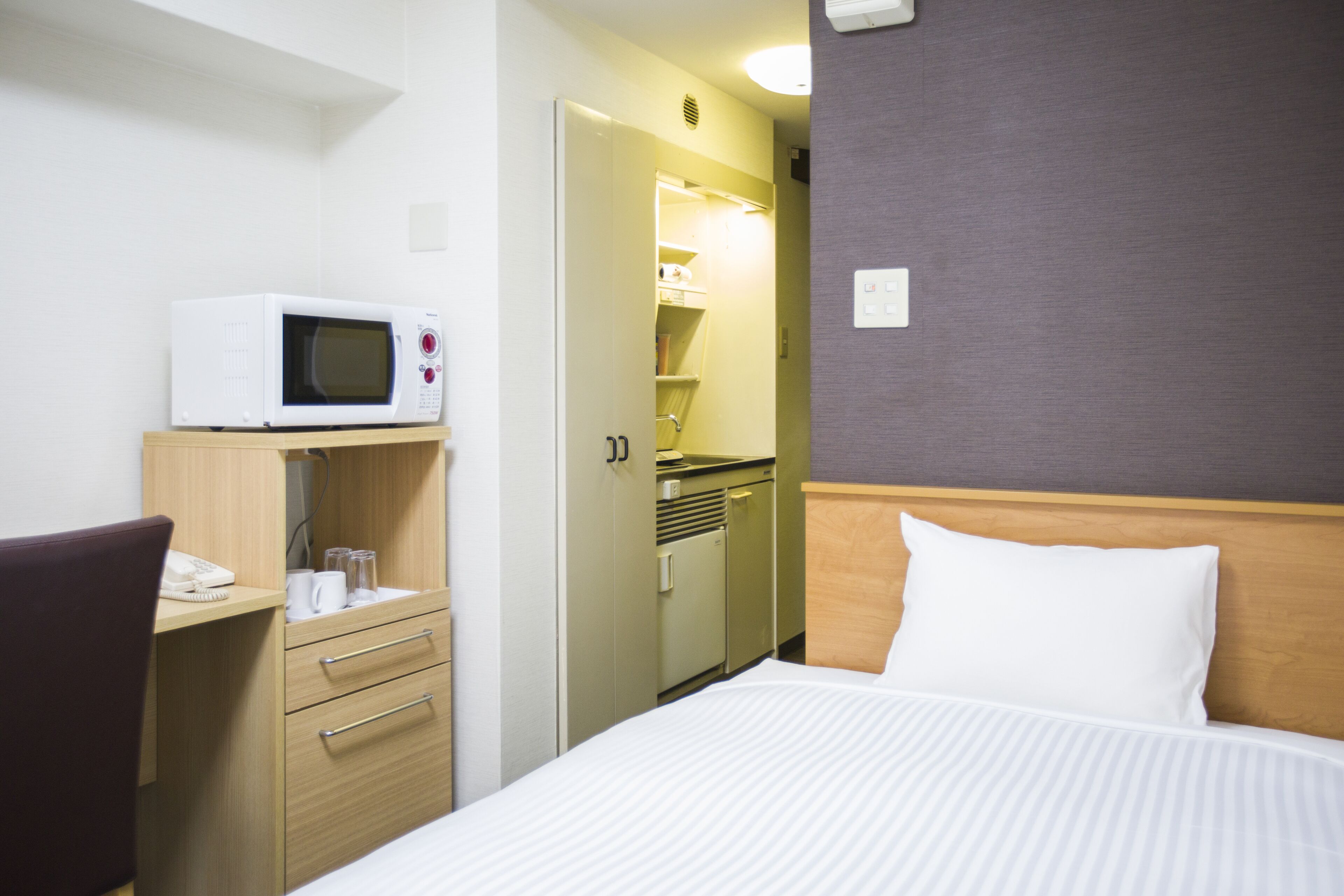 A hotel room with a bed, a desk with a microwave, a phone, and a small kitchenette.