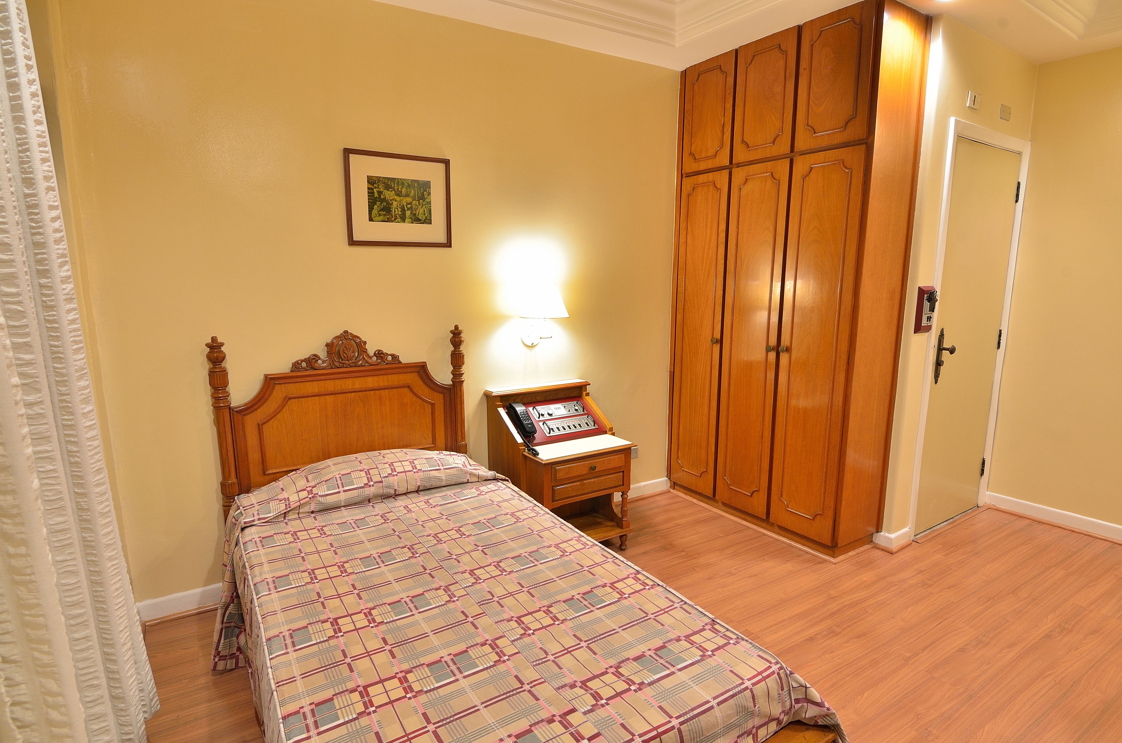 A bedroom with a bed, a nightstand, a lamp, a wardrobe, and a door.