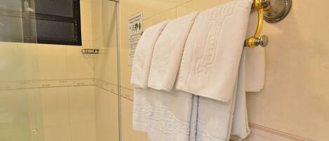 A bathroom with white tiled walls, a glass shower enclosure, and a towel rack with folded towels.