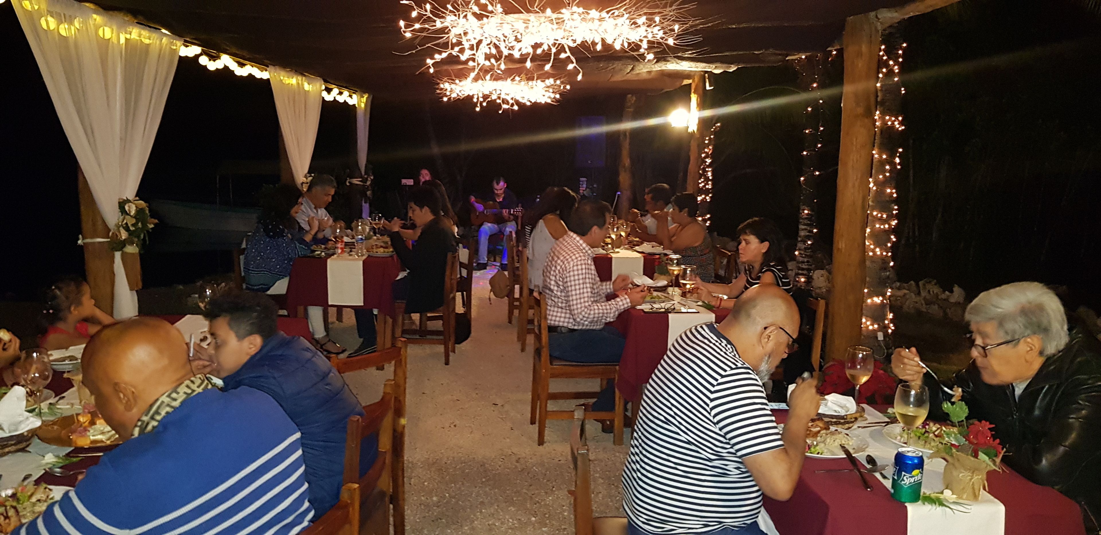 Un área de comedor al aire libre con mesas, sillas, luces colgantes y una marquesina.
