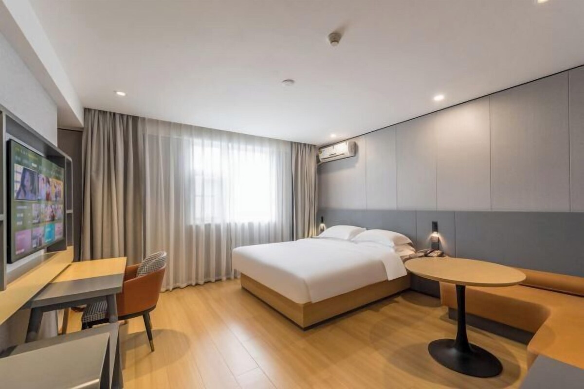 Una habitación de hotel moderna con cama, escritorio, silla, mesa redonda y televisor.