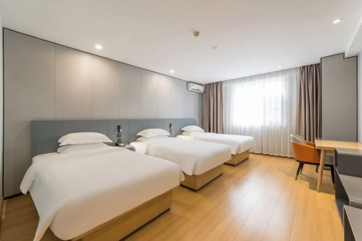 Een hotelkamer met drie bedden, een bureau en een stoel.