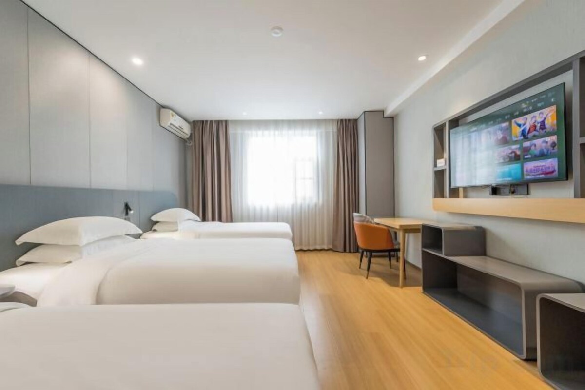 Una habitación de hotel con cama, escritorio, silla y televisión en la pared.