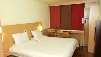 A hotel room with a bed, bedside table, lamp, and a small table with a plant.