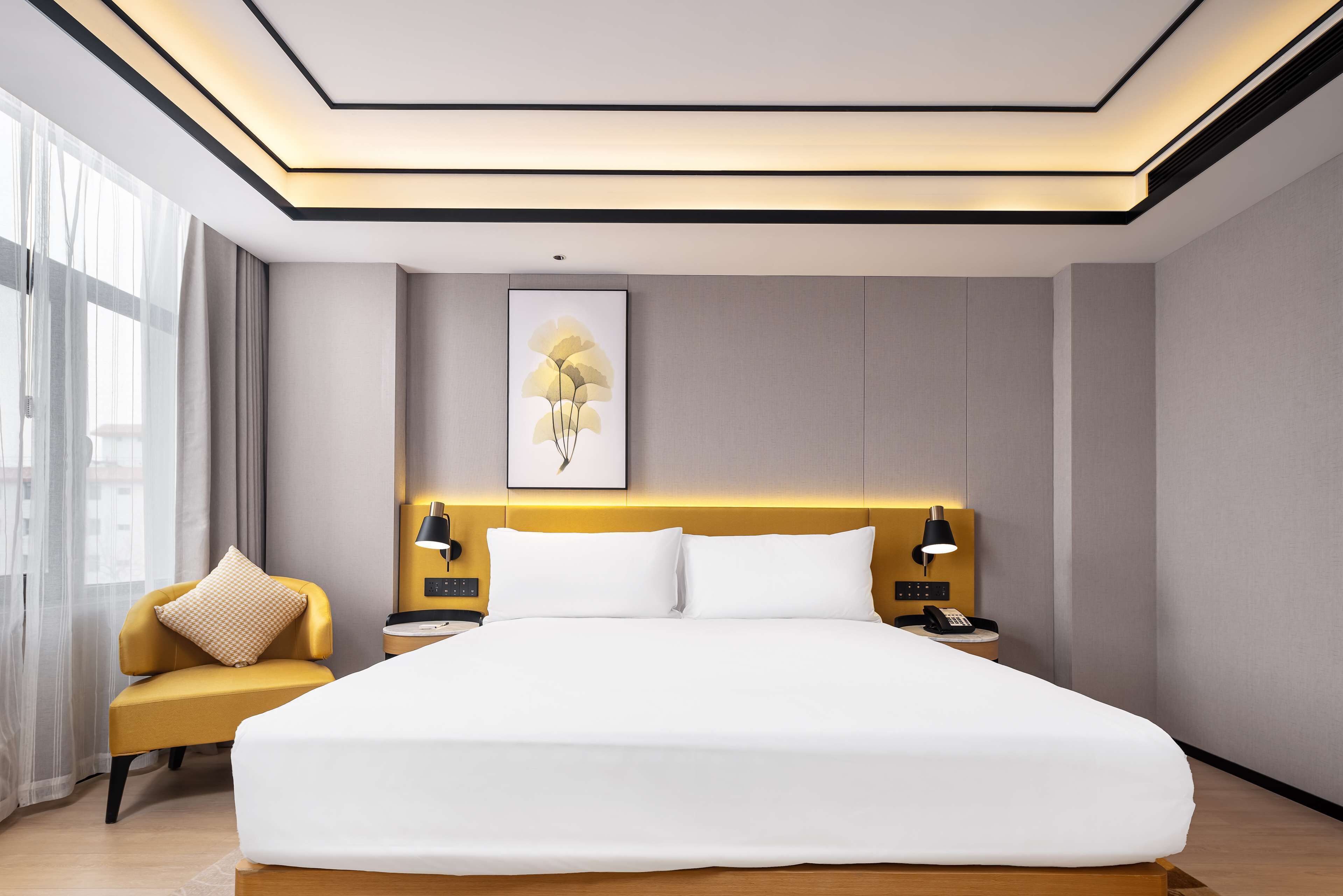 A modern hotel room with a large bed, bedside tables, a chair, and a large window.