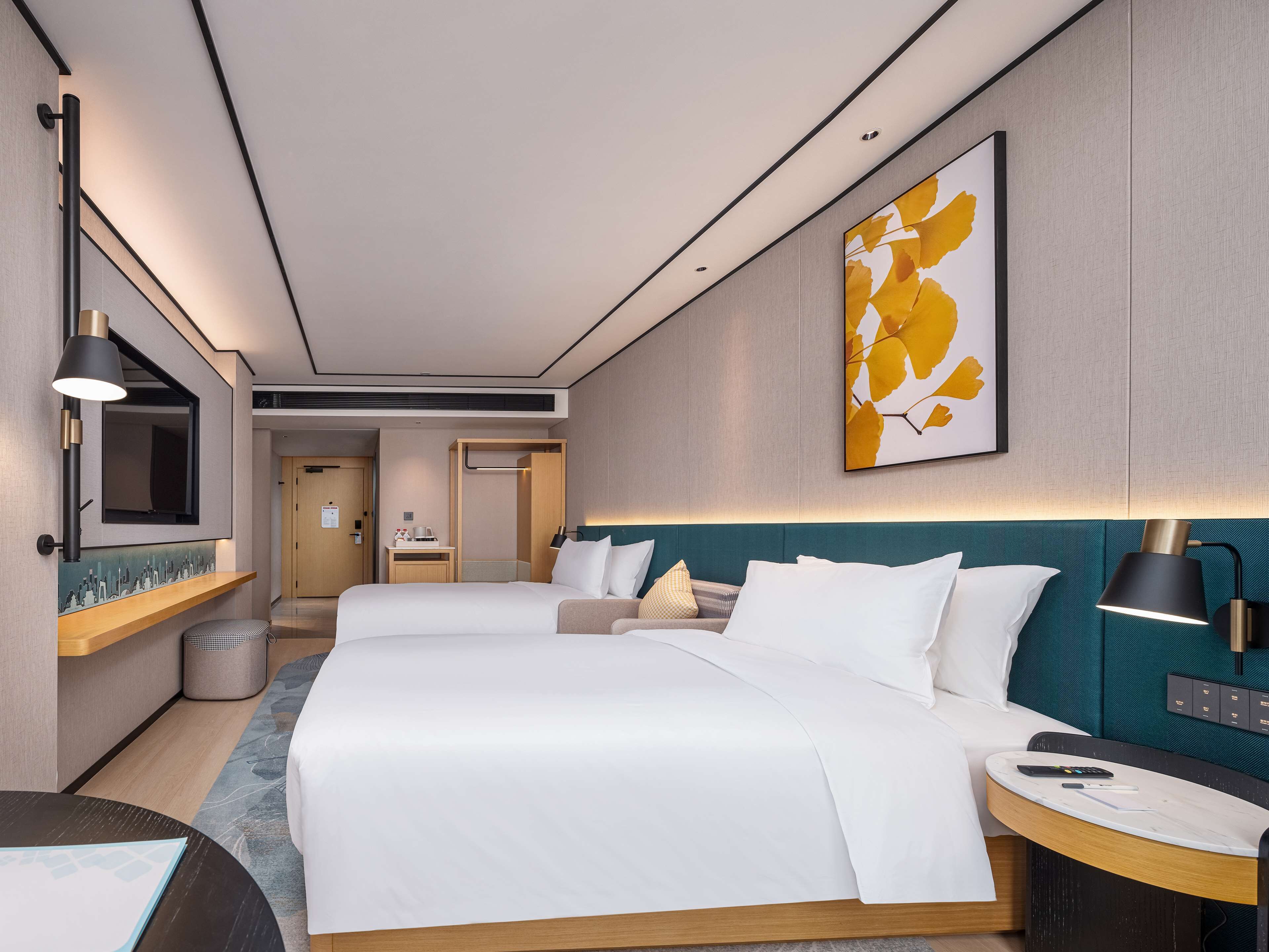 A modern hotel room with two beds, a desk, a TV, and a bathroom visible in the background.