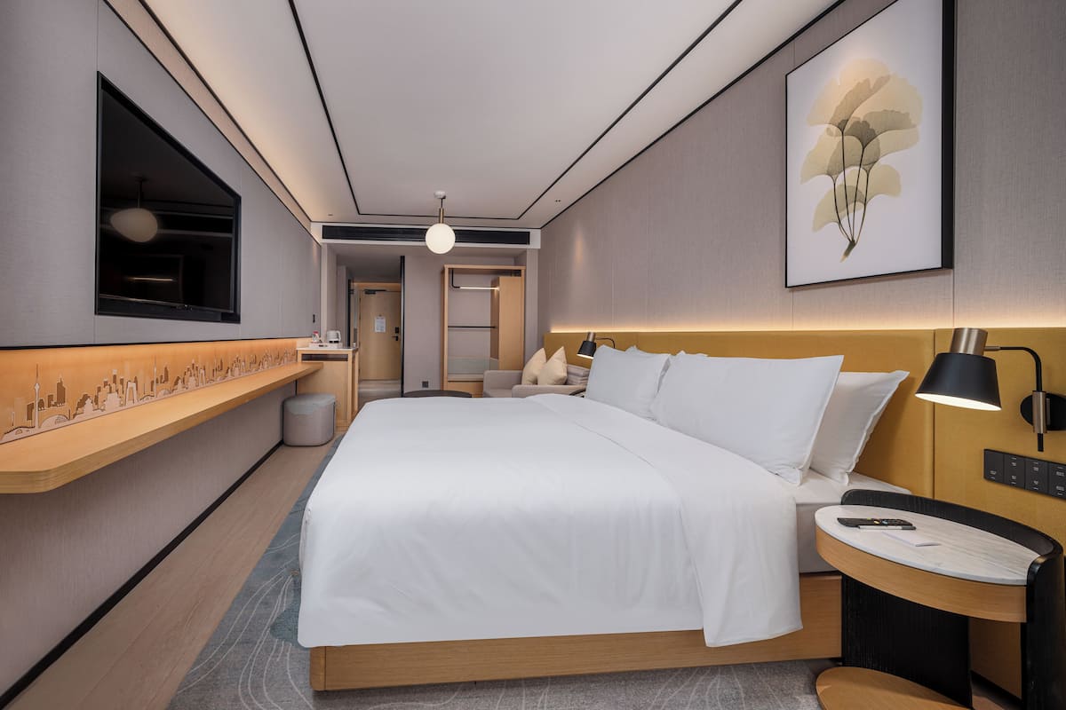 A modern hotel room with a large bed, bedside tables, a desk, and a window.