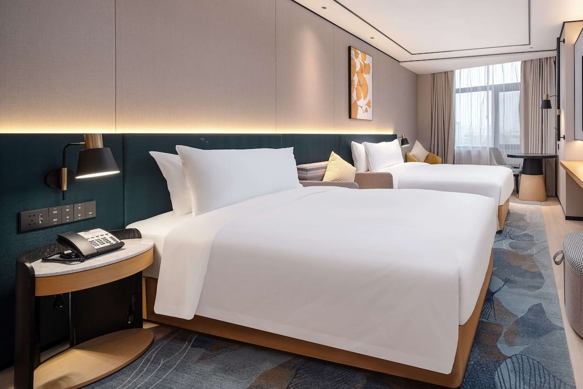 A hotel room with two beds, a desk, a chair, a phone, and a lamp.