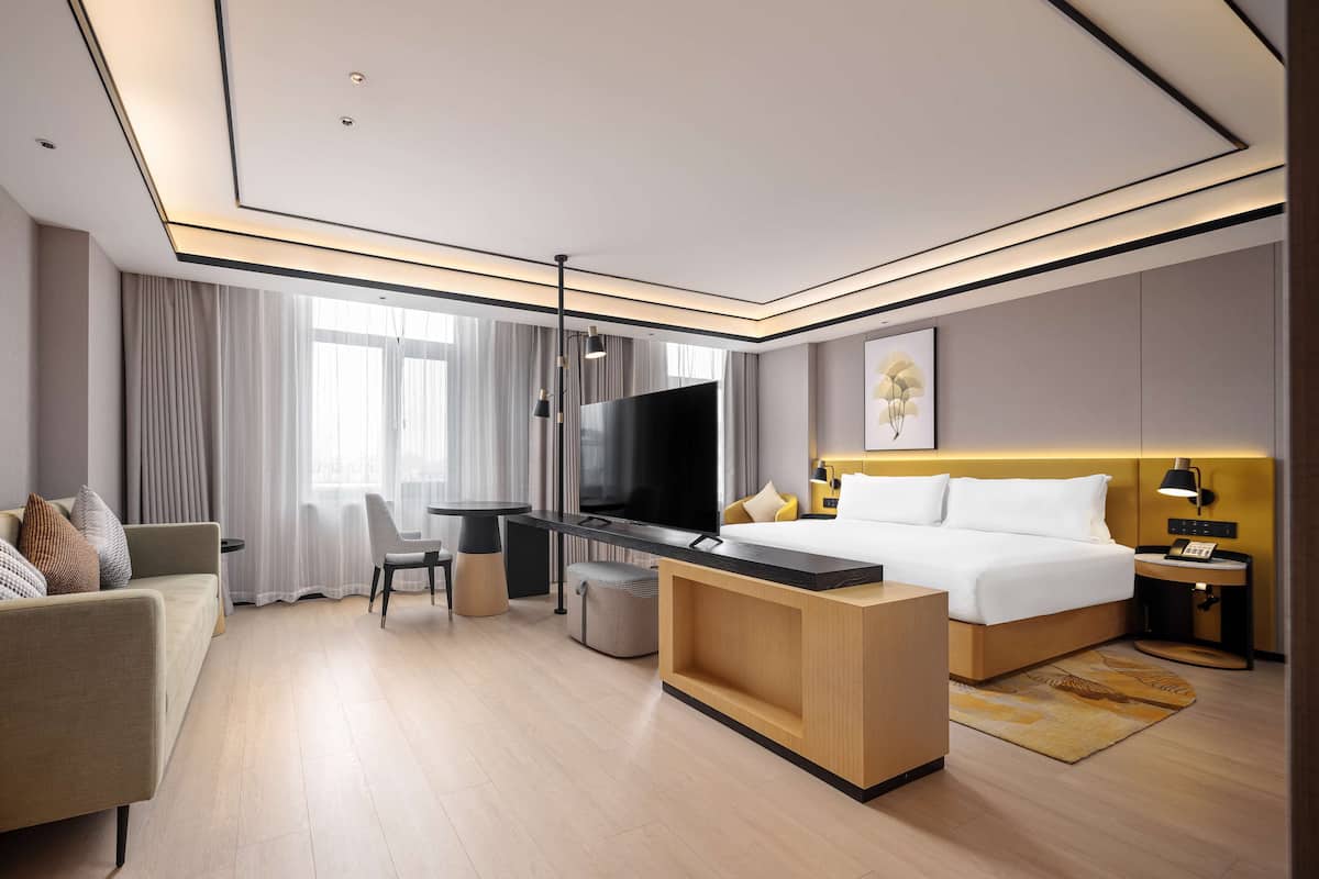 A modern hotel room with a bed, a desk, a TV, and a sofa.
