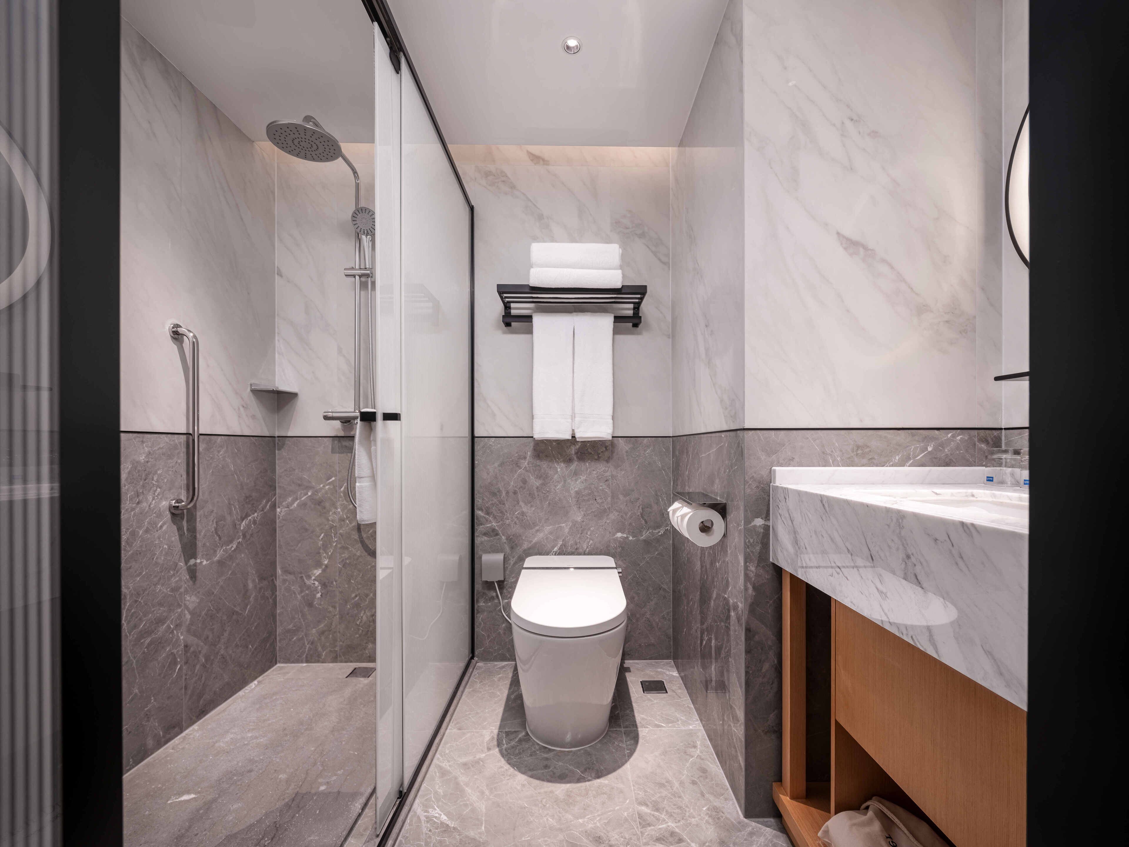 A modern bathroom with a glass-enclosed shower, a toilet, and a marble-tiled sink area.