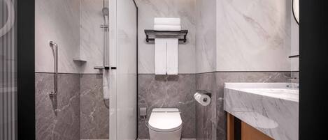 A modern bathroom with a glass-enclosed shower, a toilet, and a marble-tiled sink area.