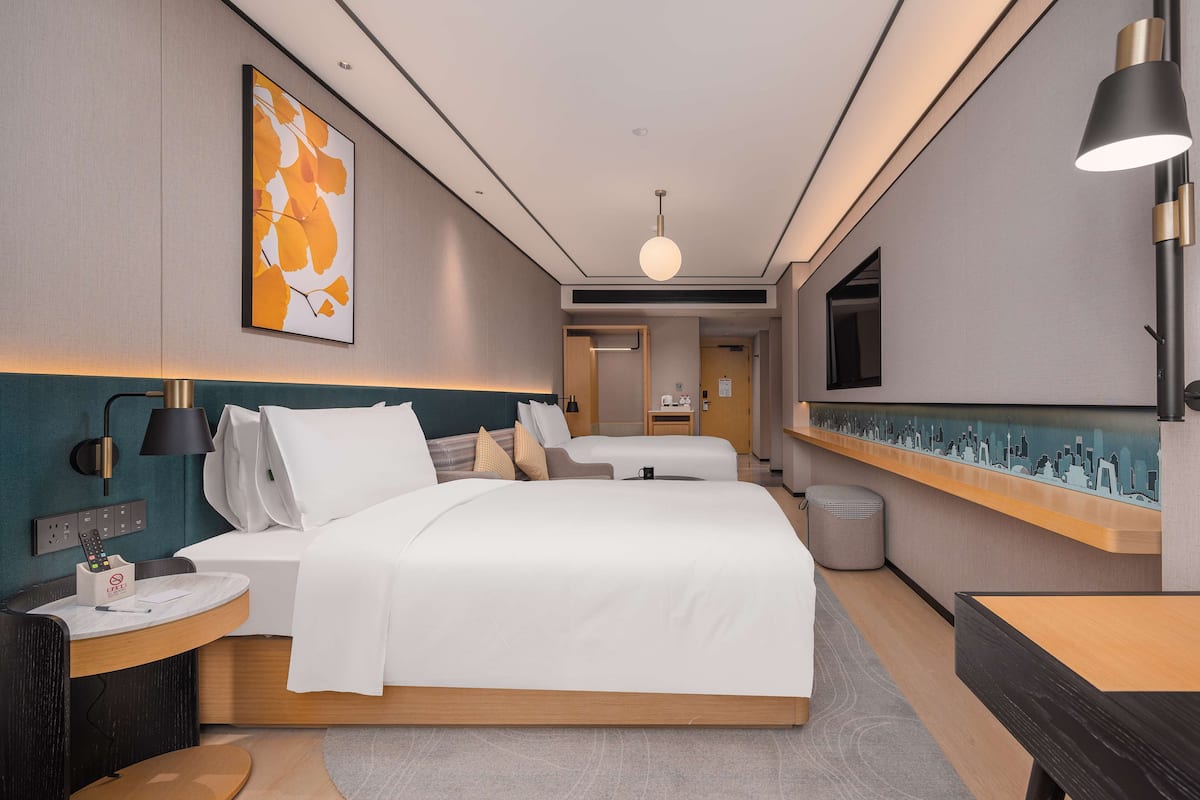 A modern hotel room with a large bed, bedside tables, a desk, and a cityscape artwork on the wall.