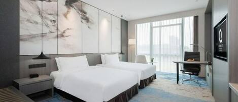 A modern hotel room with two beds, a desk, and a large window.