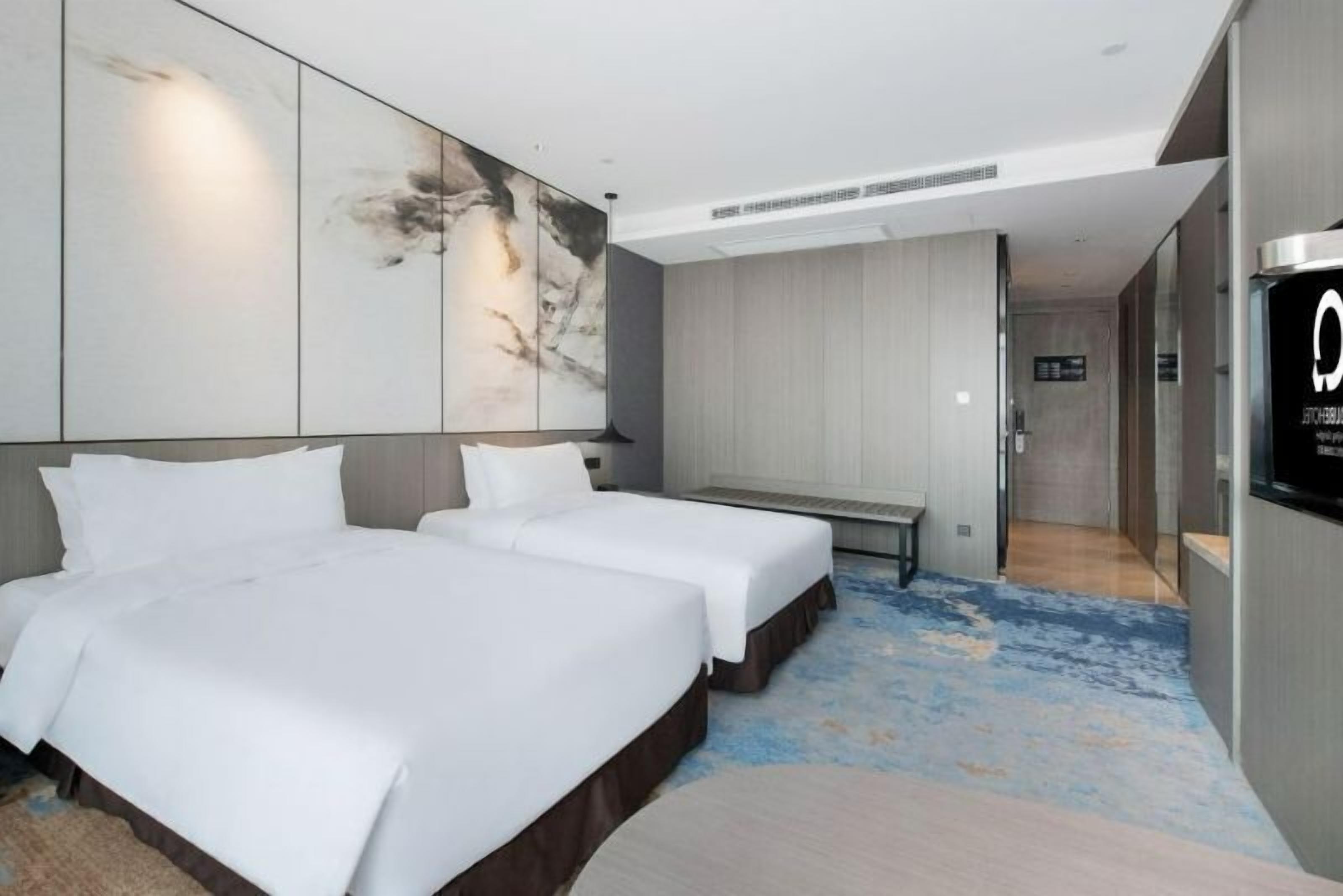 Une chambre d’hôtel avec deux lits, une grande peinture abstraite au mur, un banc et un téléviseur fixé au mur.