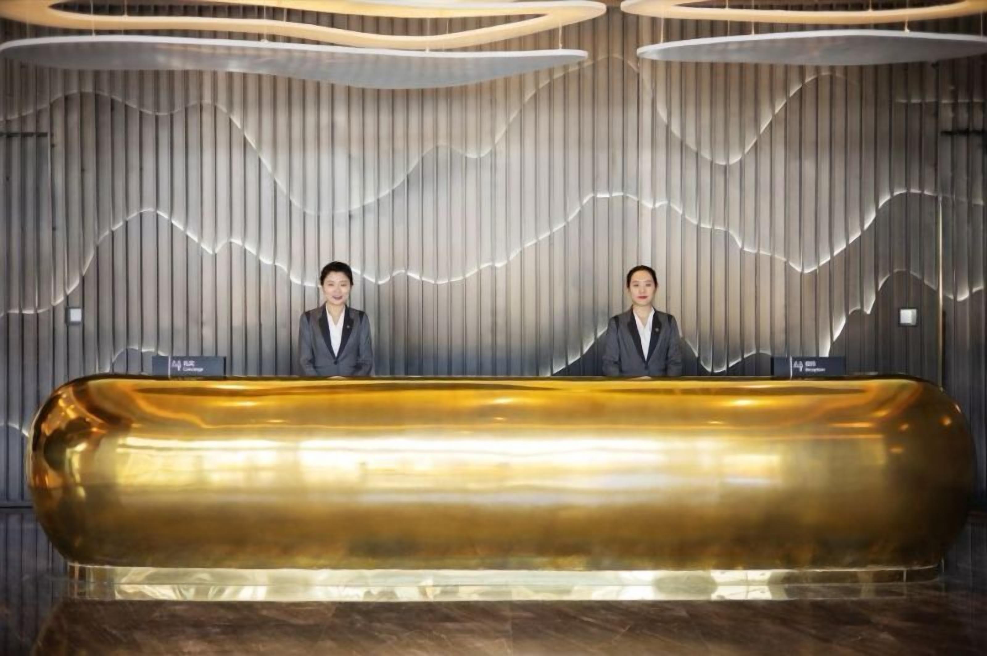 A reception desk with two attendants, a modern design with vertical lines and a wave-like pattern on the wall, and a golden reception counter.