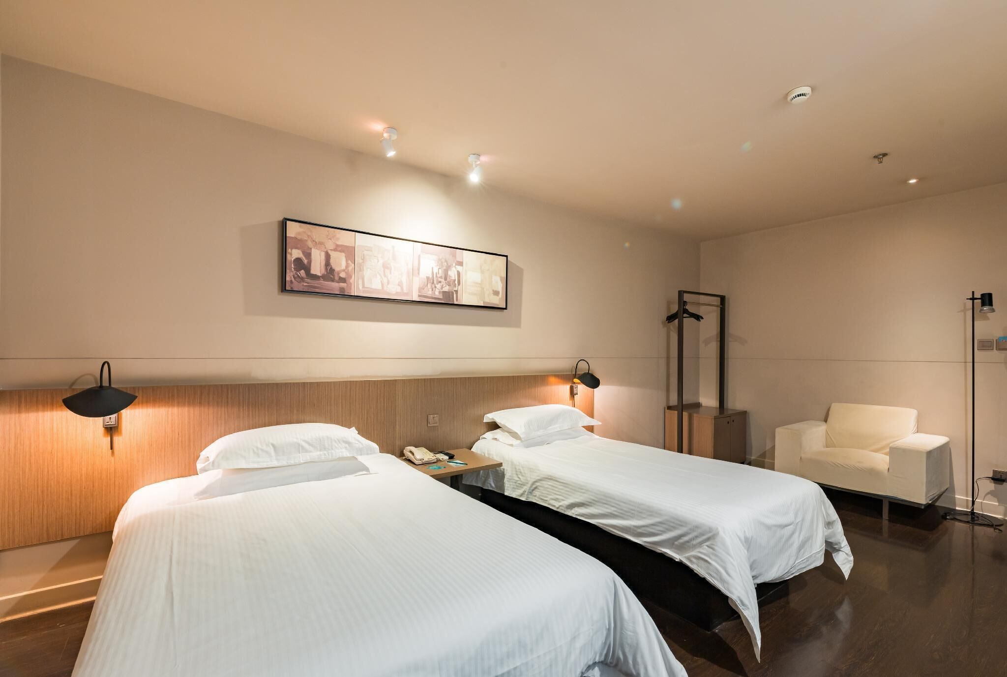 Habitación de hotel con dos camas, un escritorio, una silla, un perchero y un cuadro en la pared.