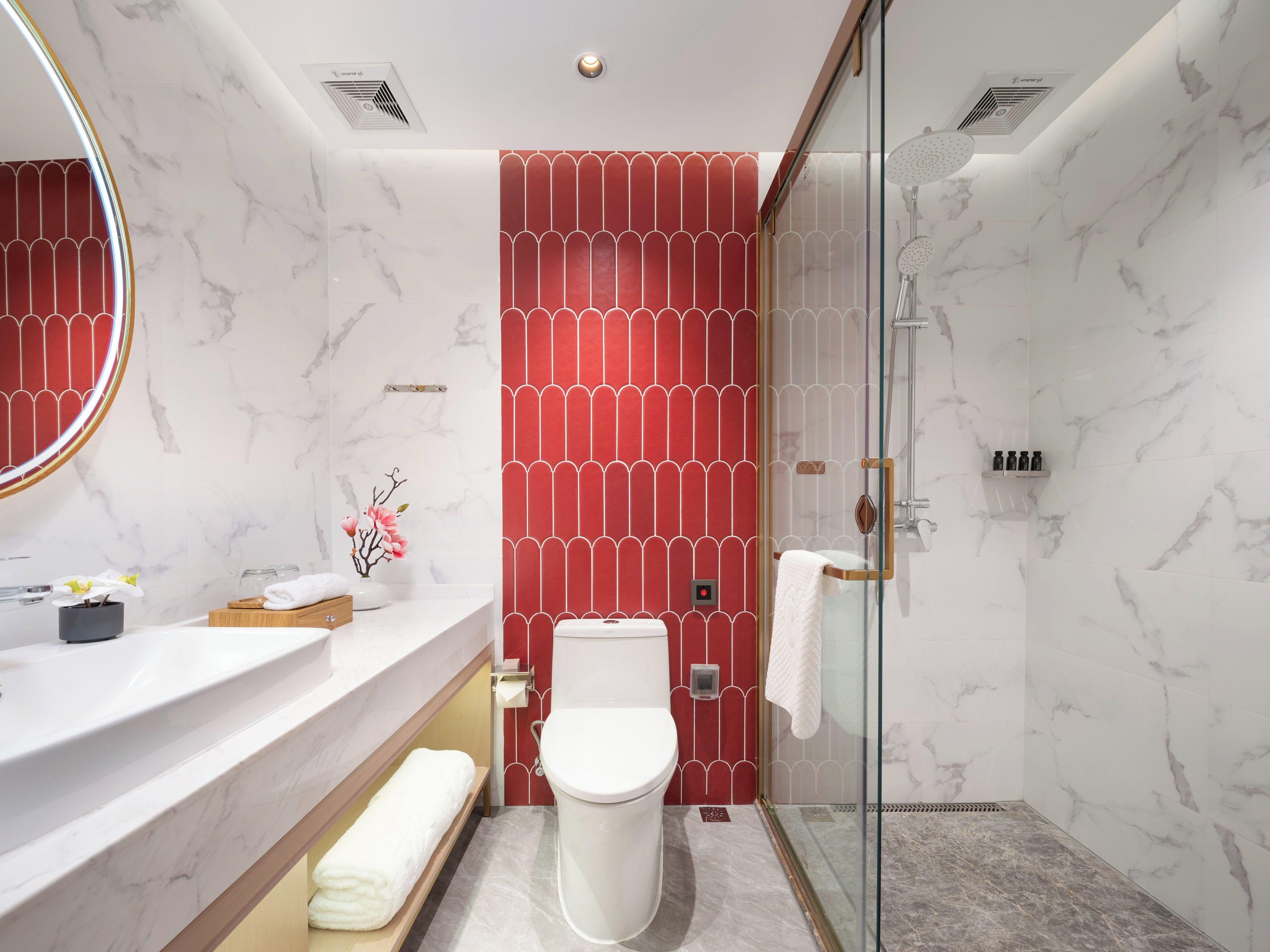 A modern bathroom with a marble floor, a white toilet, a glass shower enclosure, and a red patterned wall.
