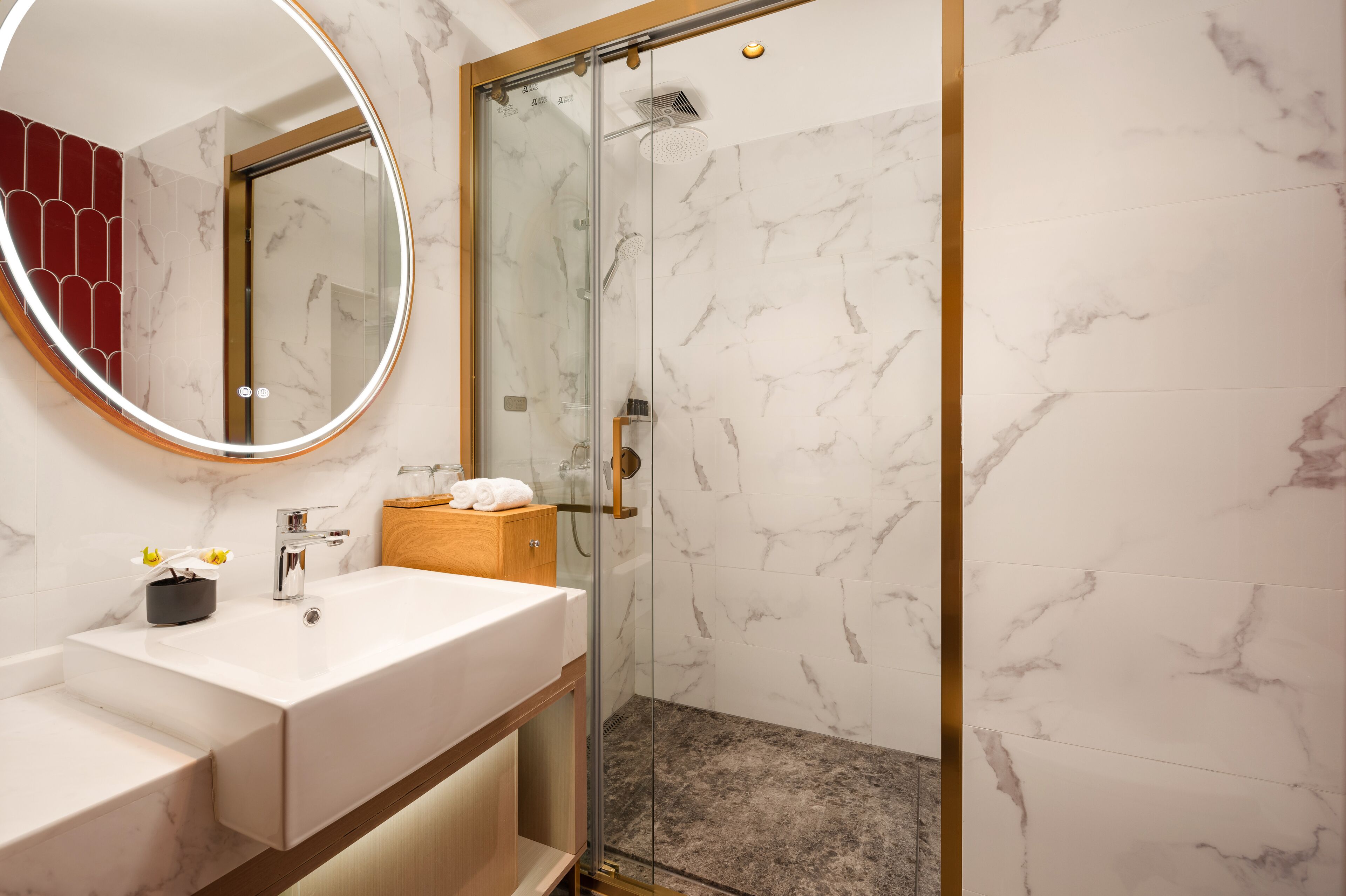 A modern bathroom with a marble vanity, a glass shower enclosure, and a wooden cabinet.