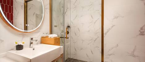 A modern bathroom with a marble vanity, a glass shower enclosure, and a wooden cabinet.