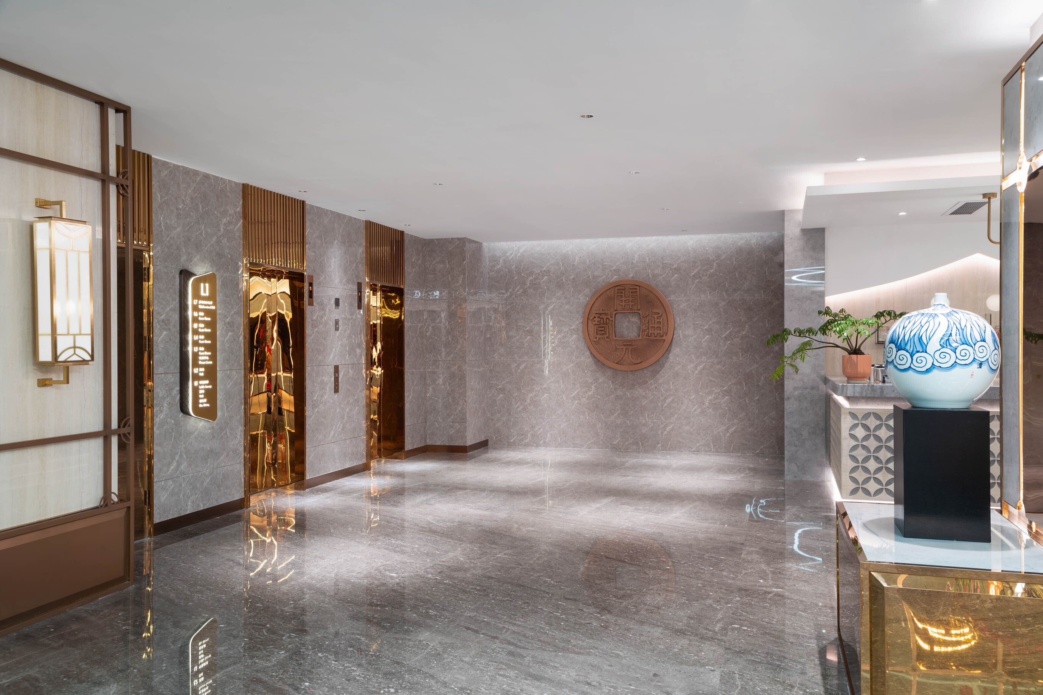 A modern hotel lobby with a marble floor, a reception desk, and a large decorative vase.