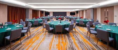 A large conference room with multiple round tables, each set with chairs and table settings.