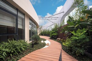 A modern building with a curved wooden pathway surrounded by lush greenery and a clear blue sky.