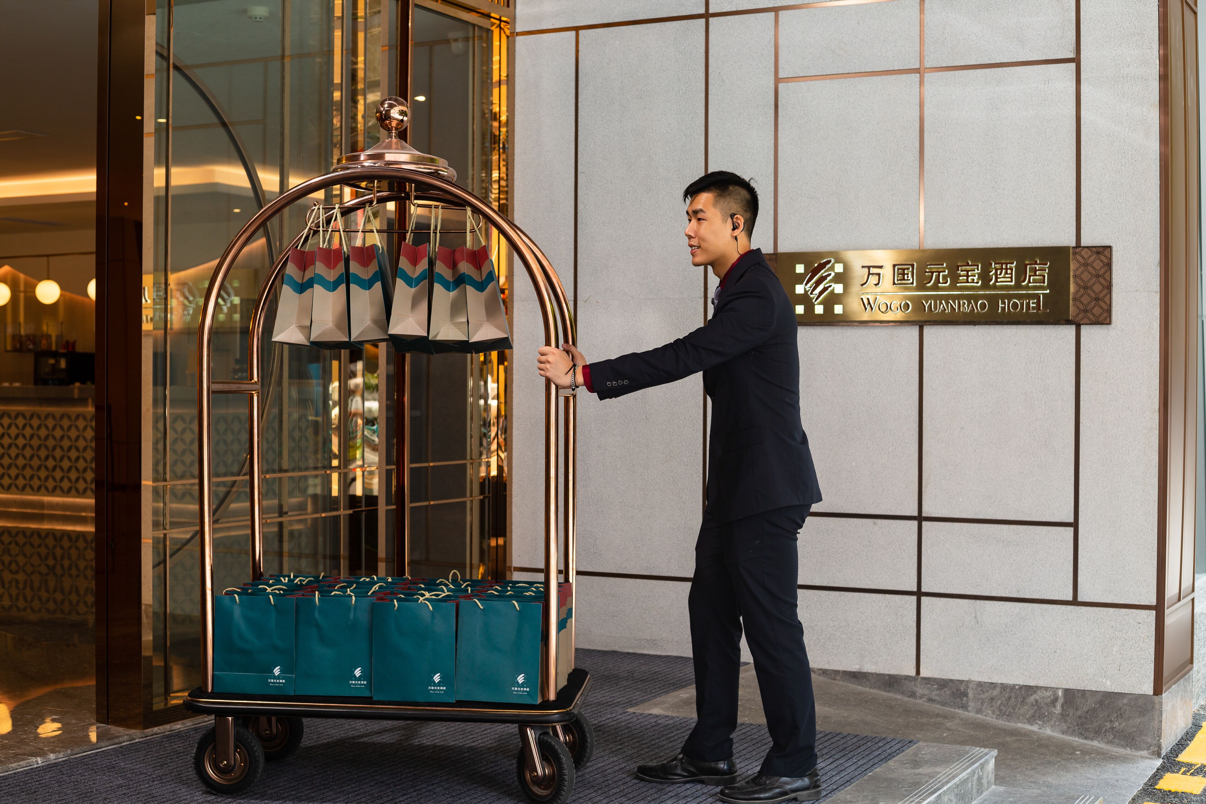 Un hombre empuja un carrito de equipaje con maletas frente a la entrada de un hotel.