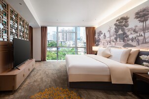 Una camera d'albergo moderna con un letto grande, una TV a schermo piatto, vista sulla città e un murale decorativo.