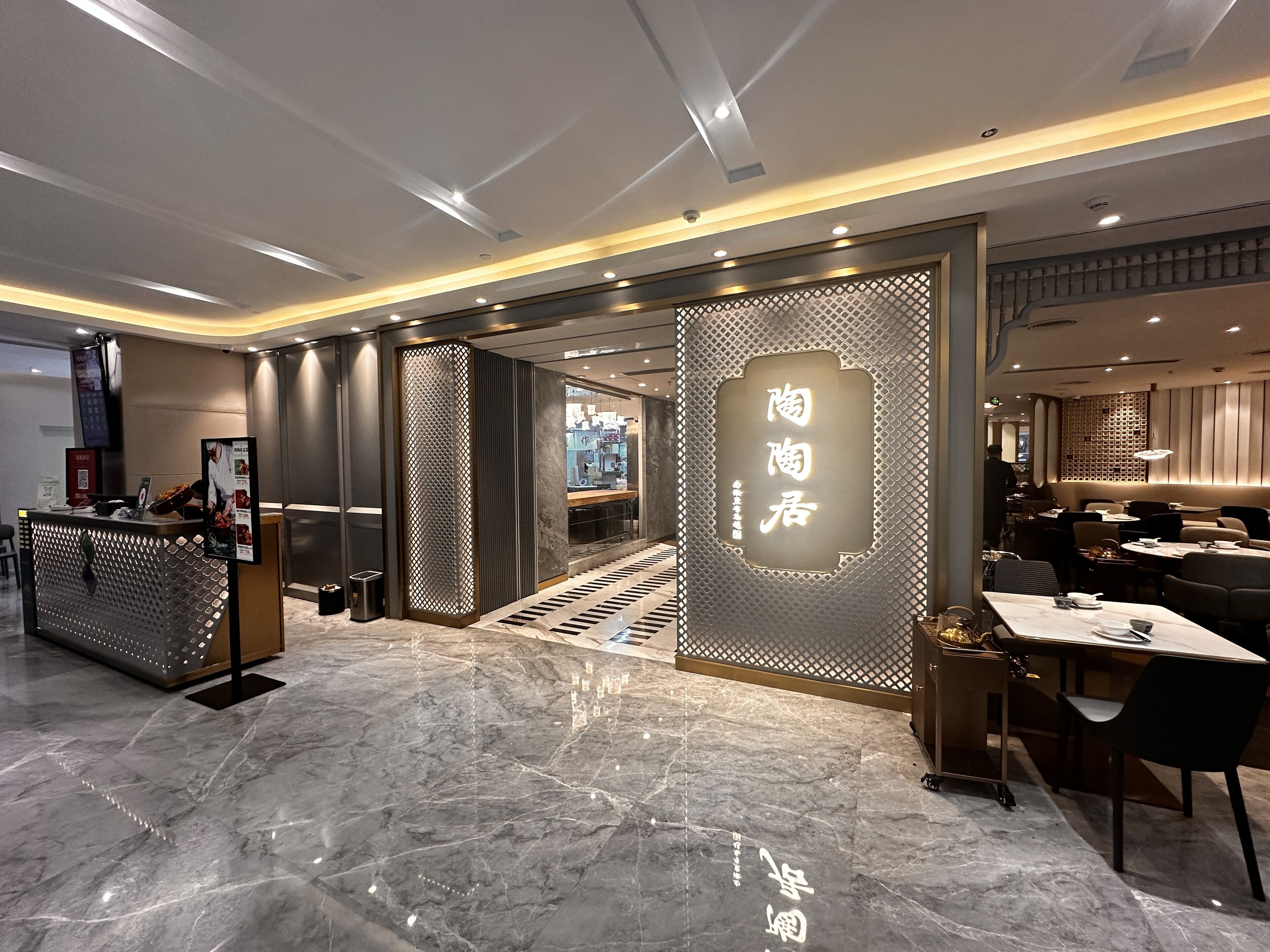 A modern restaurant interior with a marble floor, a reception desk, and a dining area with tables and chairs.
