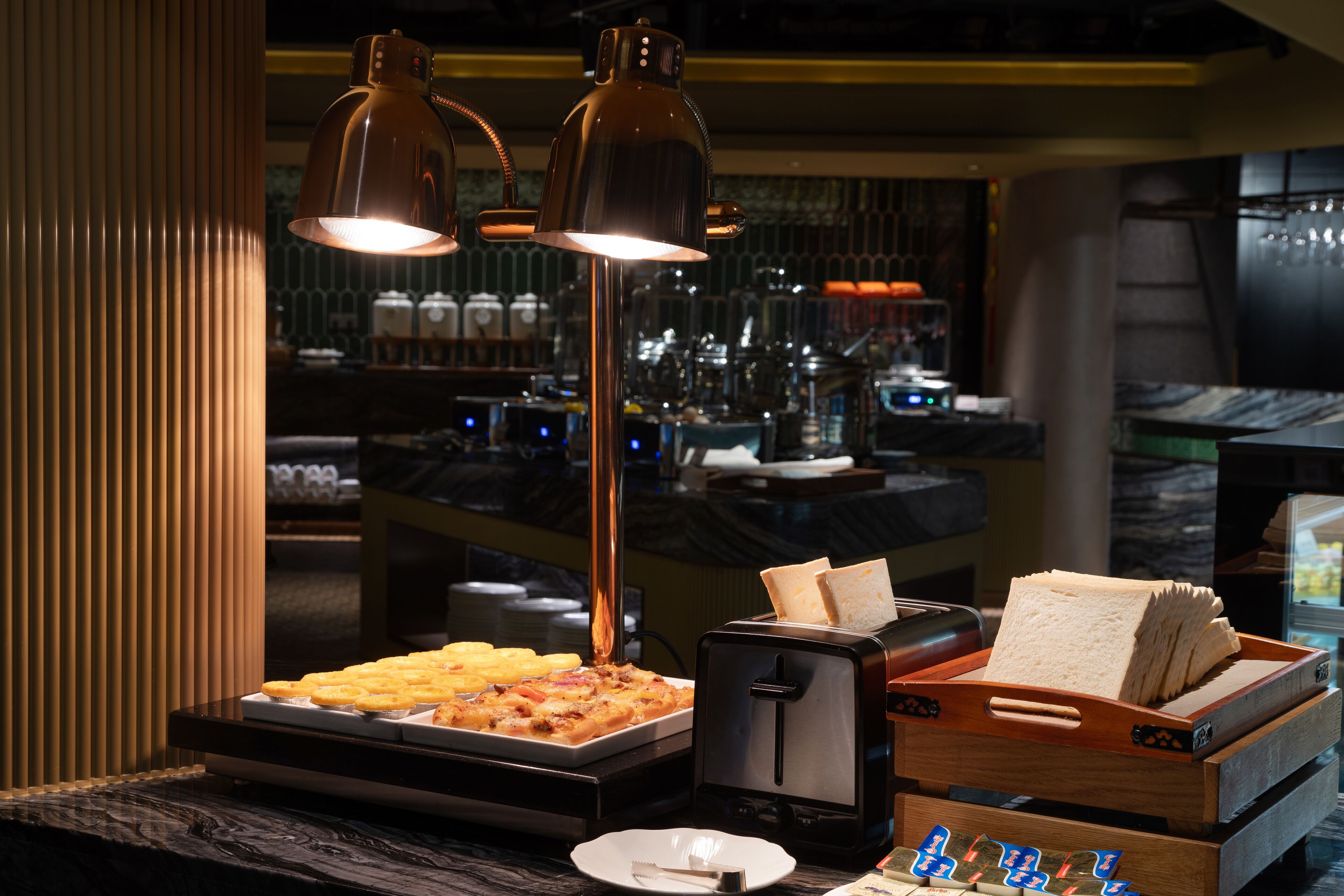 A buffet setup with a tray of food, a toaster, and a bread basket.