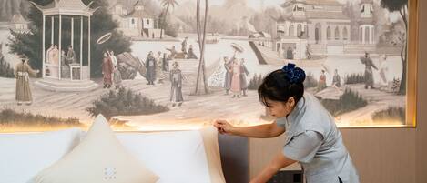 Una habitación de hotel con cama, televisor montado en la pared y un mural que representa una escena tradicional.