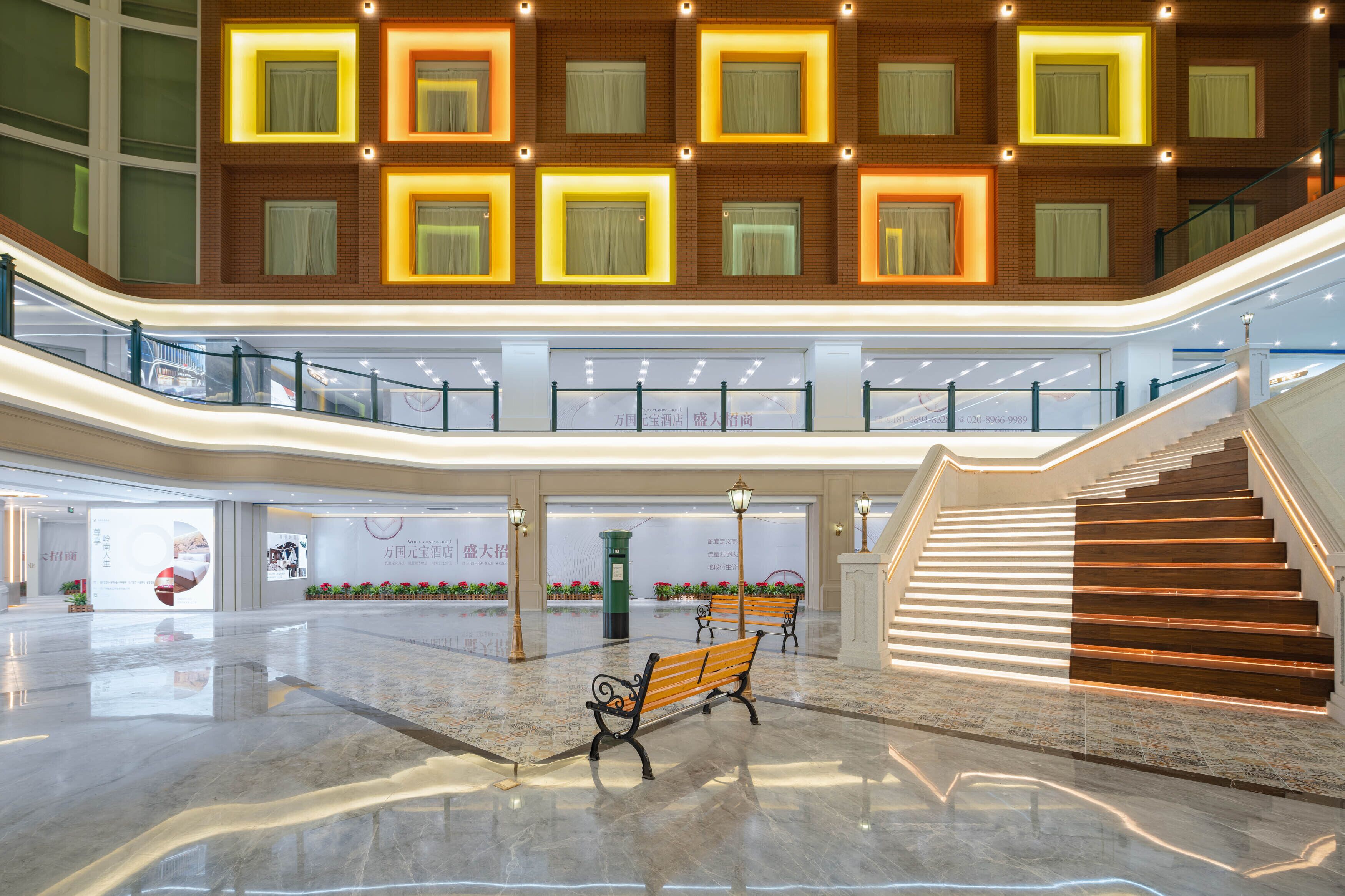 A spacious atrium with a central staircase, benches, and a modern design with illuminated windows.