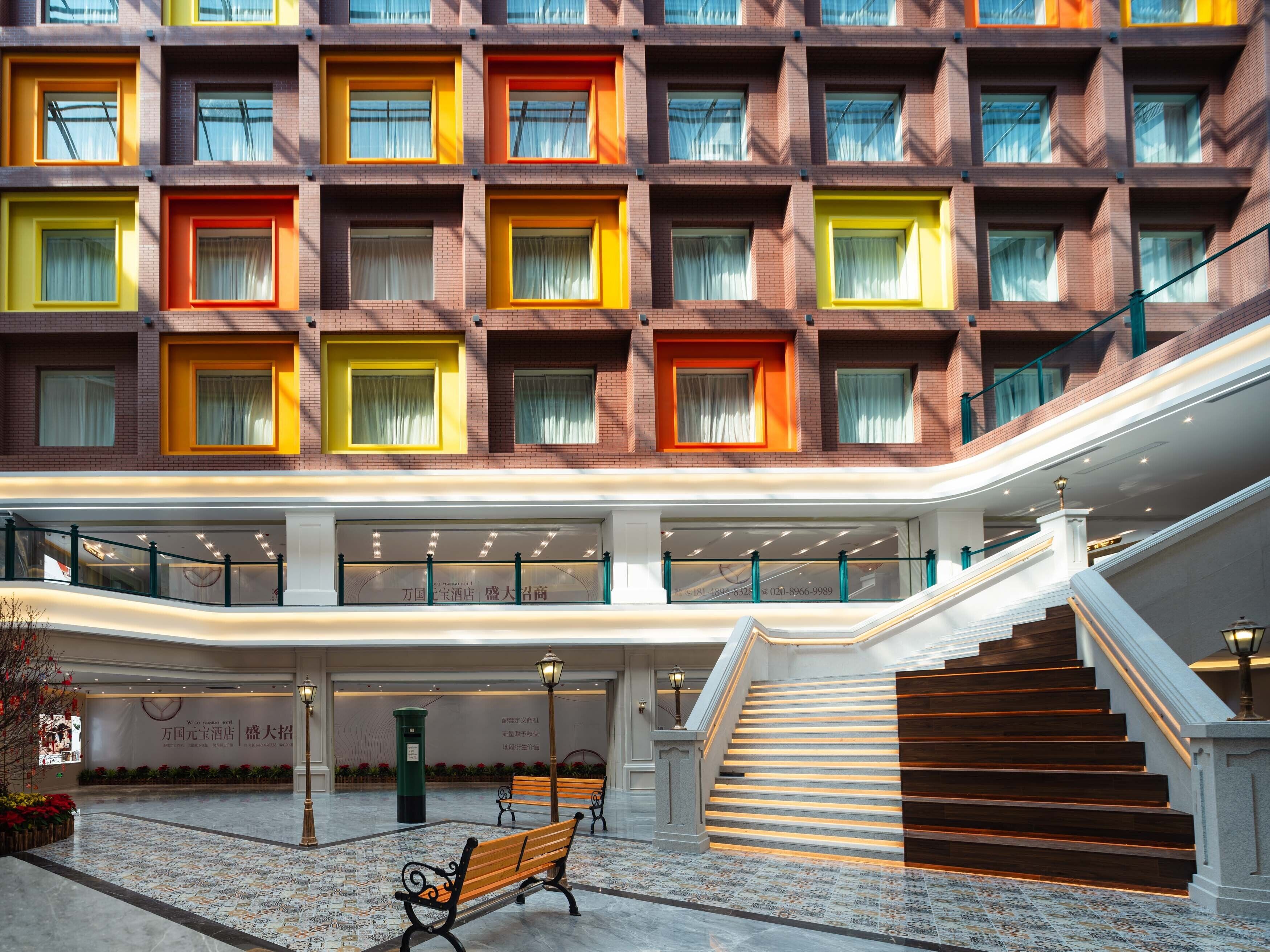 A hotel lobby with a central staircase, multiple floors, and a large window with curtains.