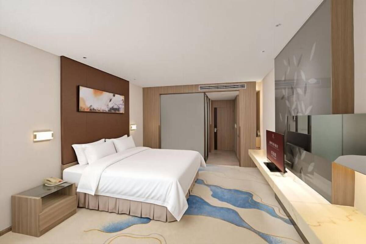 Een hotelkamer met een groot bed, een bureau met telefoon, een flatscreen-televisie en een deur naar een andere kamer.