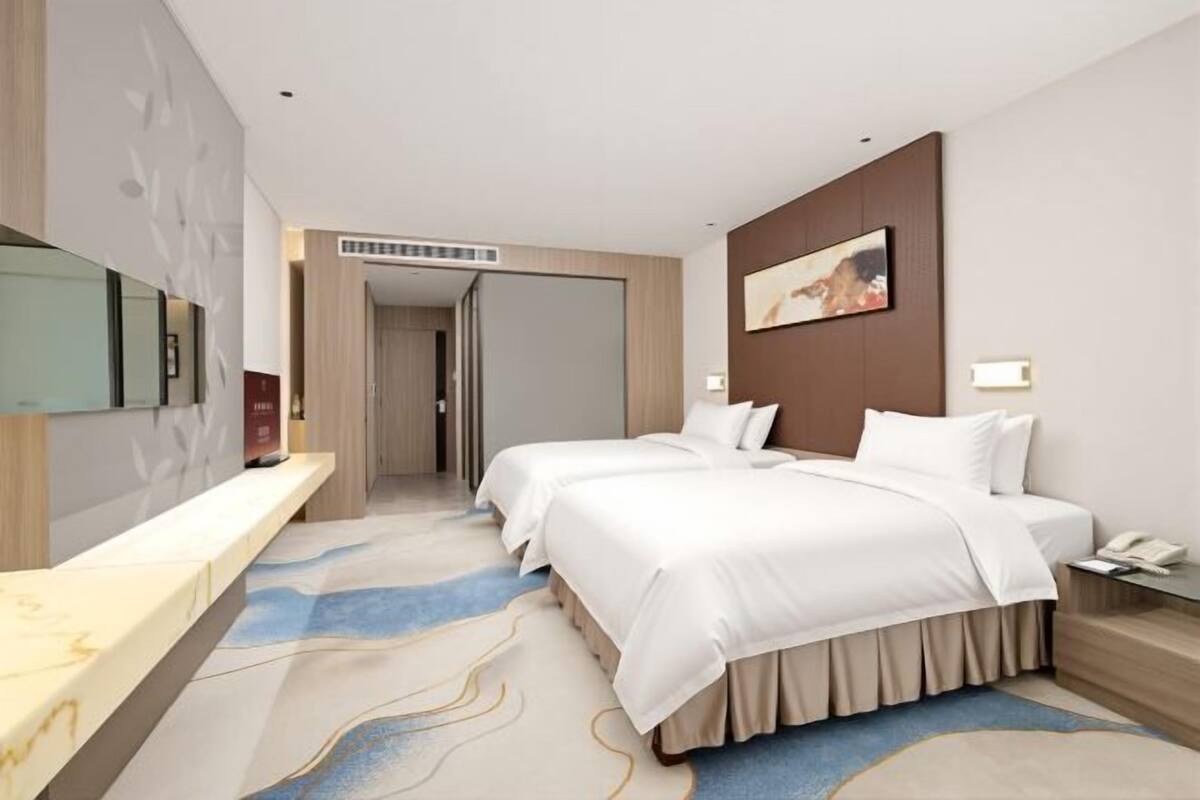 Een hotelkamer met twee bedden, een bureau, een spiegel, een schilderij en een deur die naar een andere kamer leidt.