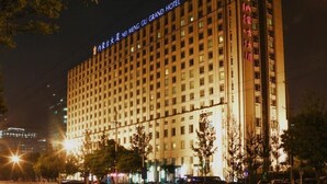A multi-story hotel building with illuminated signage, a prominent entrance, and a surrounding urban street at night. - Inner Mongolia Grand Hotel (Beijing)