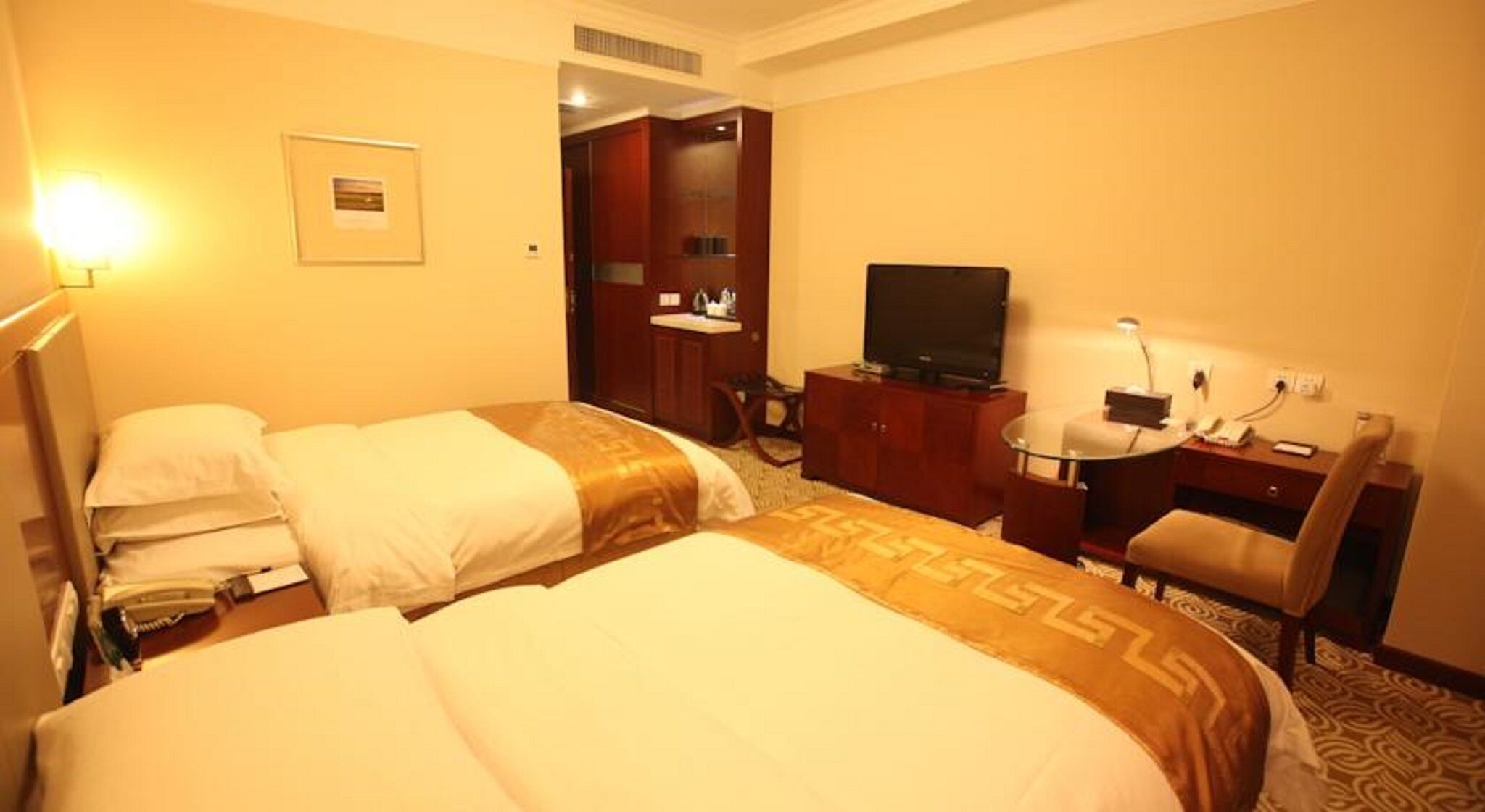 A hotel room with two beds, a desk with a chair, a television, and a small desk lamp.