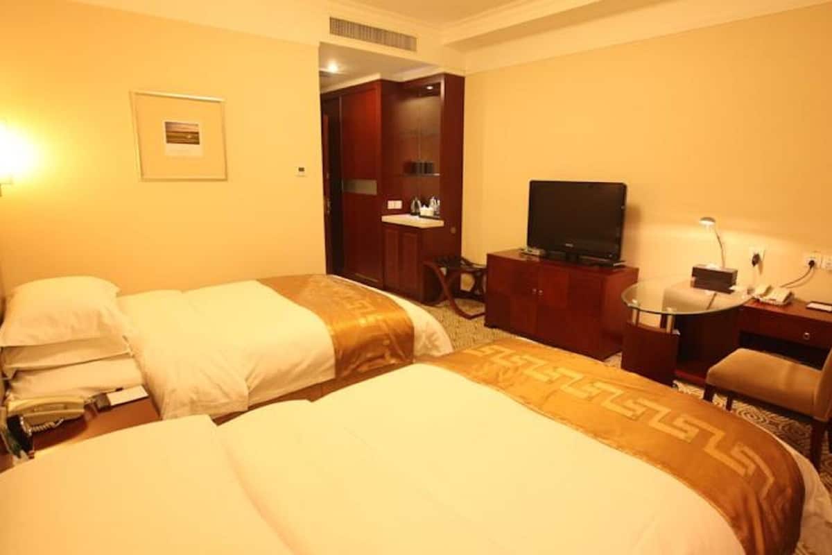 Une chambre d’hôtel avec deux lits, un bureau avec une chaise, une télévision et une petite lampe de bureau.