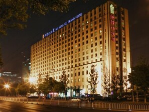 Edifício de hotel com vários andares, fachada iluminada, entrada destacada e rua urbana ao redor à noite.