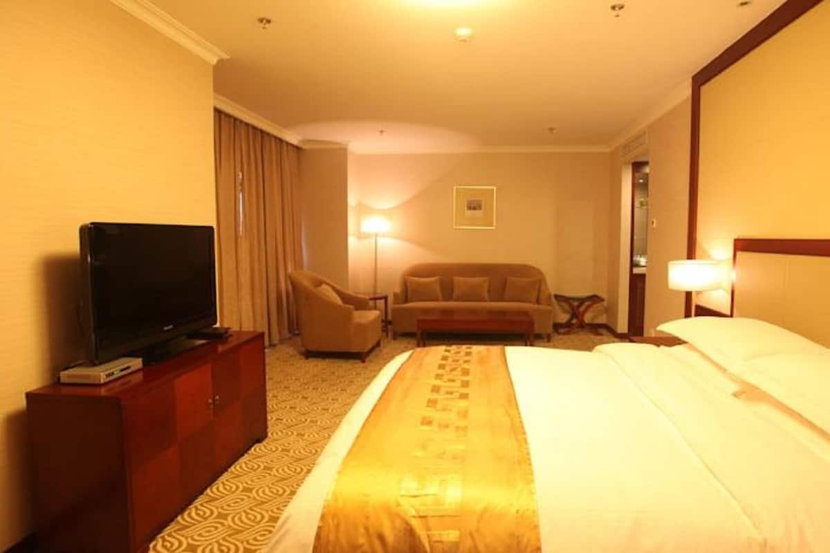Une chambre d’hôtel avec un lit, un téléviseur posé sur une commode en bois, un canapé, un bureau et une lampe.
