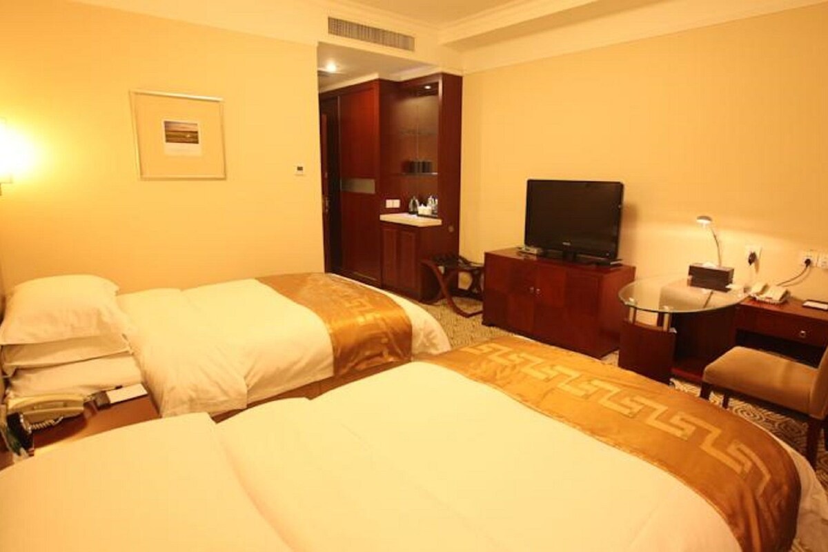 A hotel room with two beds, a desk with a chair, a television, and a small desk lamp.