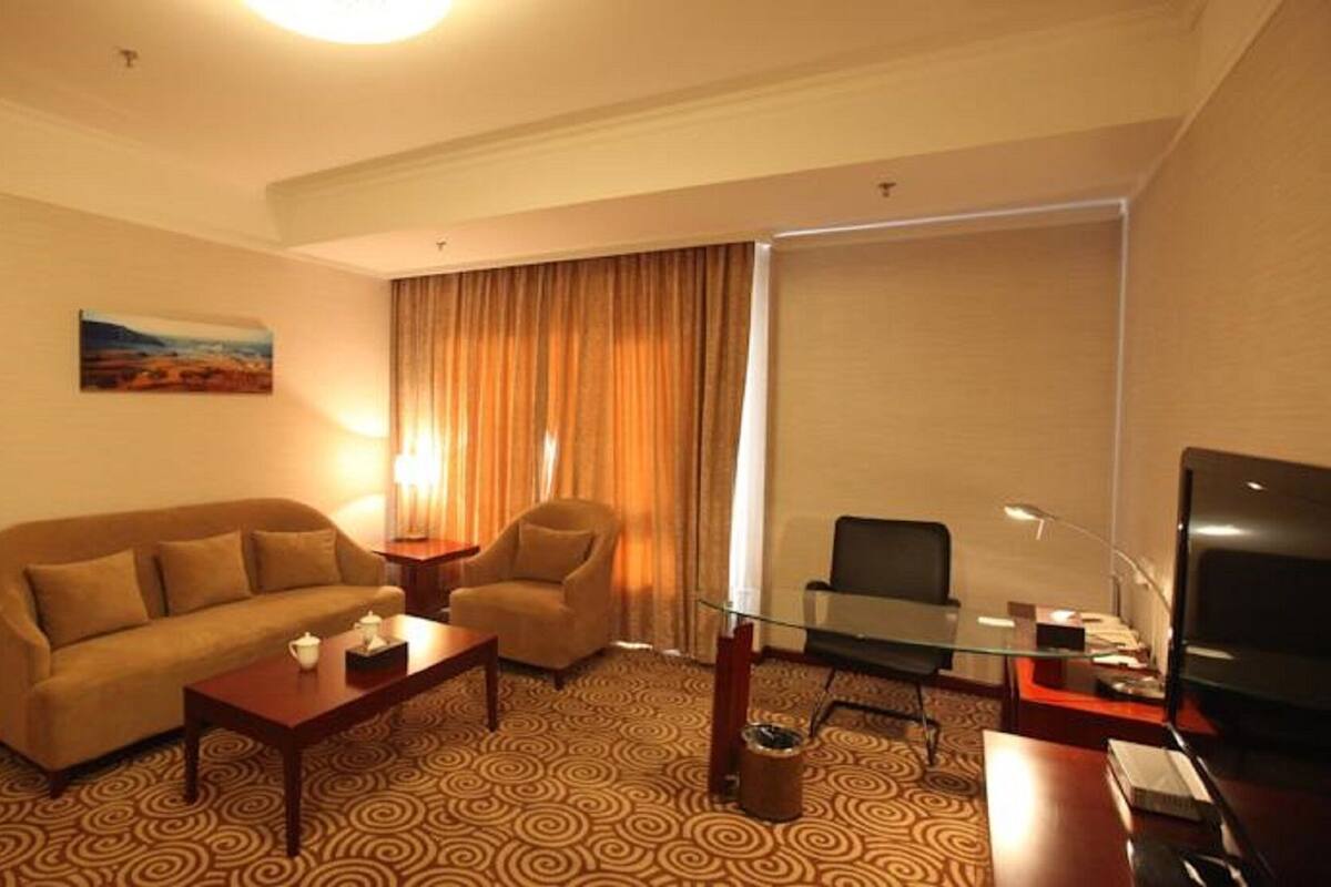 Une chambre d’hôtel avec un canapé, un fauteuil, une table basse, une télévision et un tableau au mur.