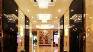 A hotel lobby with a chandelier, elevators, a patterned floor, and a large poster. - Inner Mongolia Grand Hotel (Beijing)