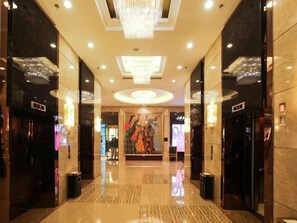 A hotel lobby with a chandelier, elevators, a patterned floor, and a large poster. - Inner Mongolia Grand Hotel (Beijing)